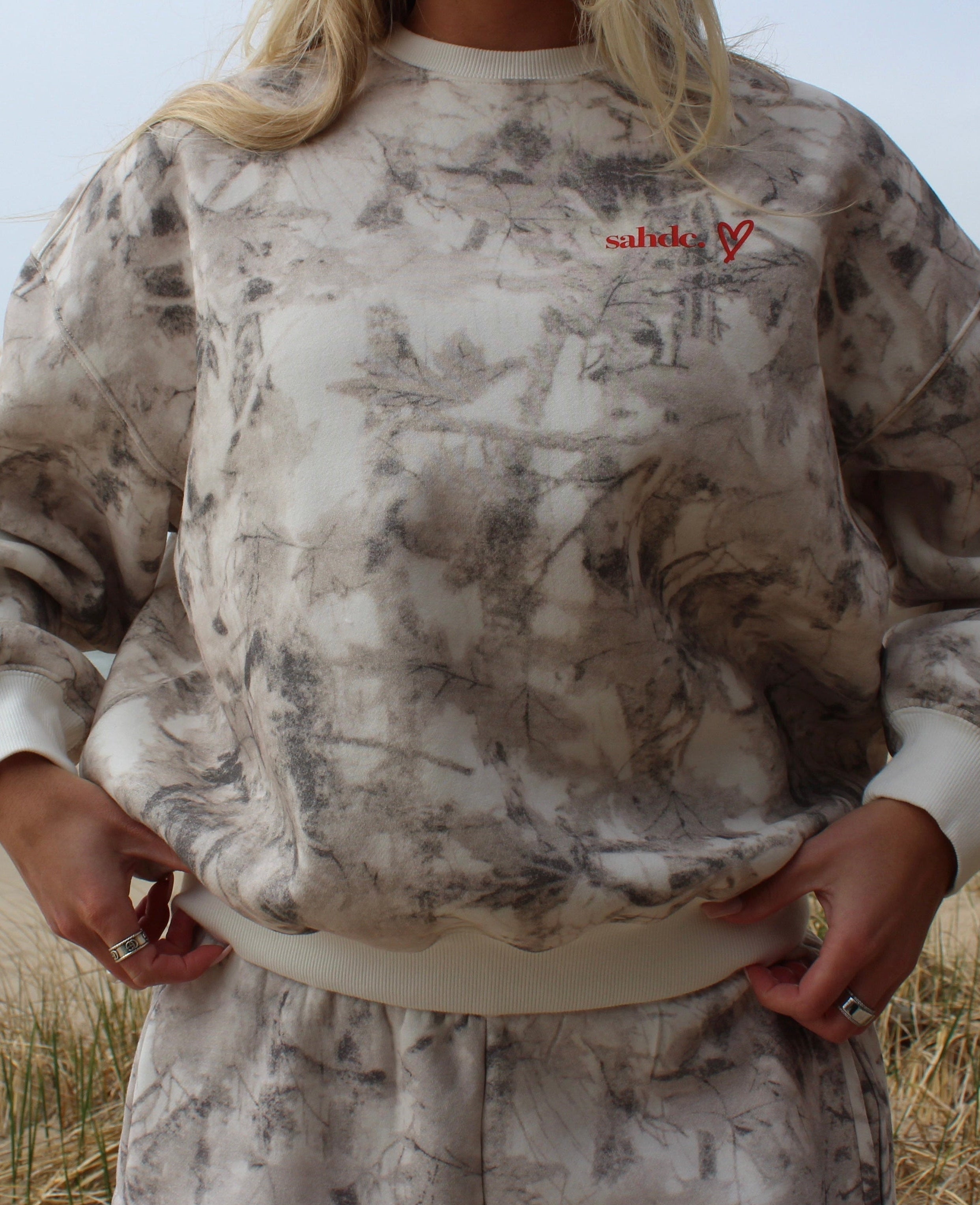Person wearing a camouflage sweatshirt with visible branding on a beach.