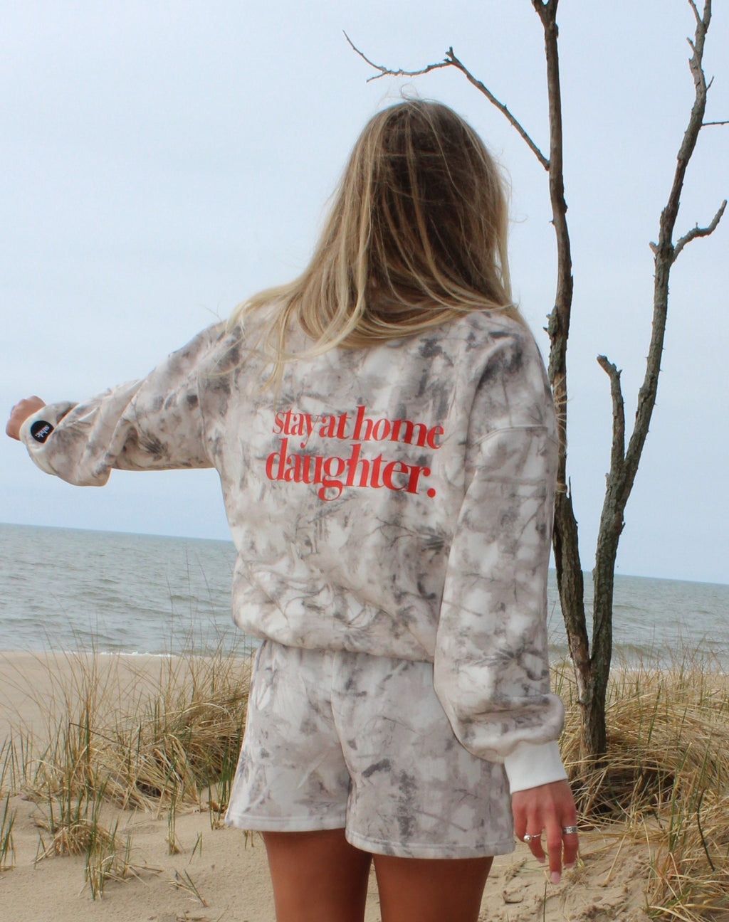 Person standing on a sandy beach with ocean view, wearing a camo set 