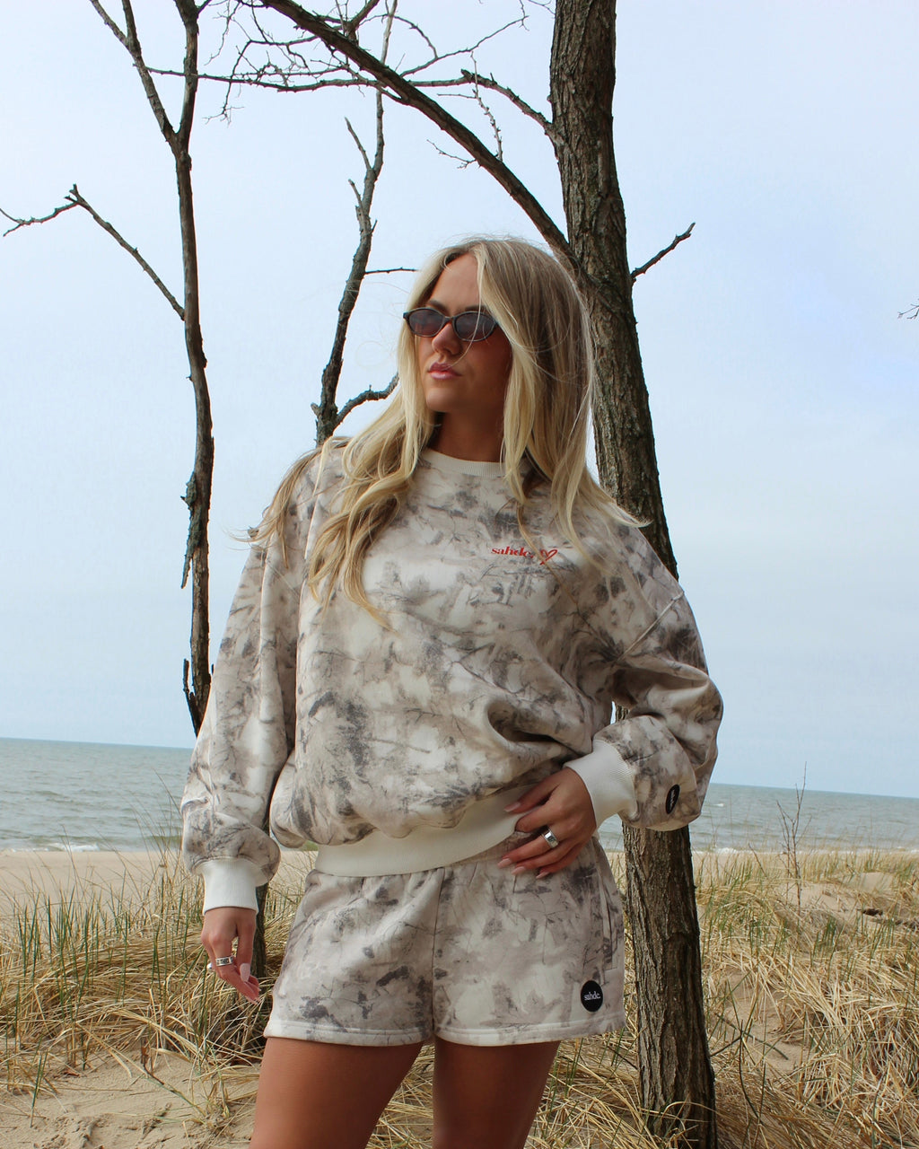 Woman in a camo set standing on a beach with trees in the background