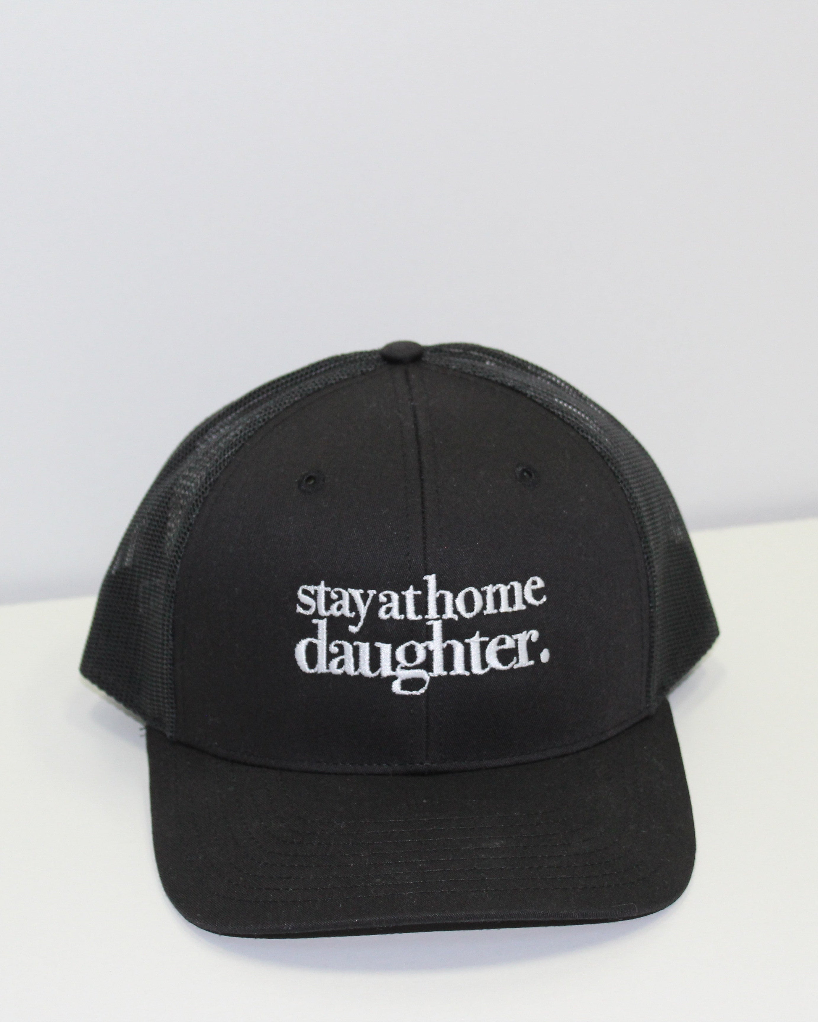 Black cap with 'stayathome.daughter.' text on a white surface