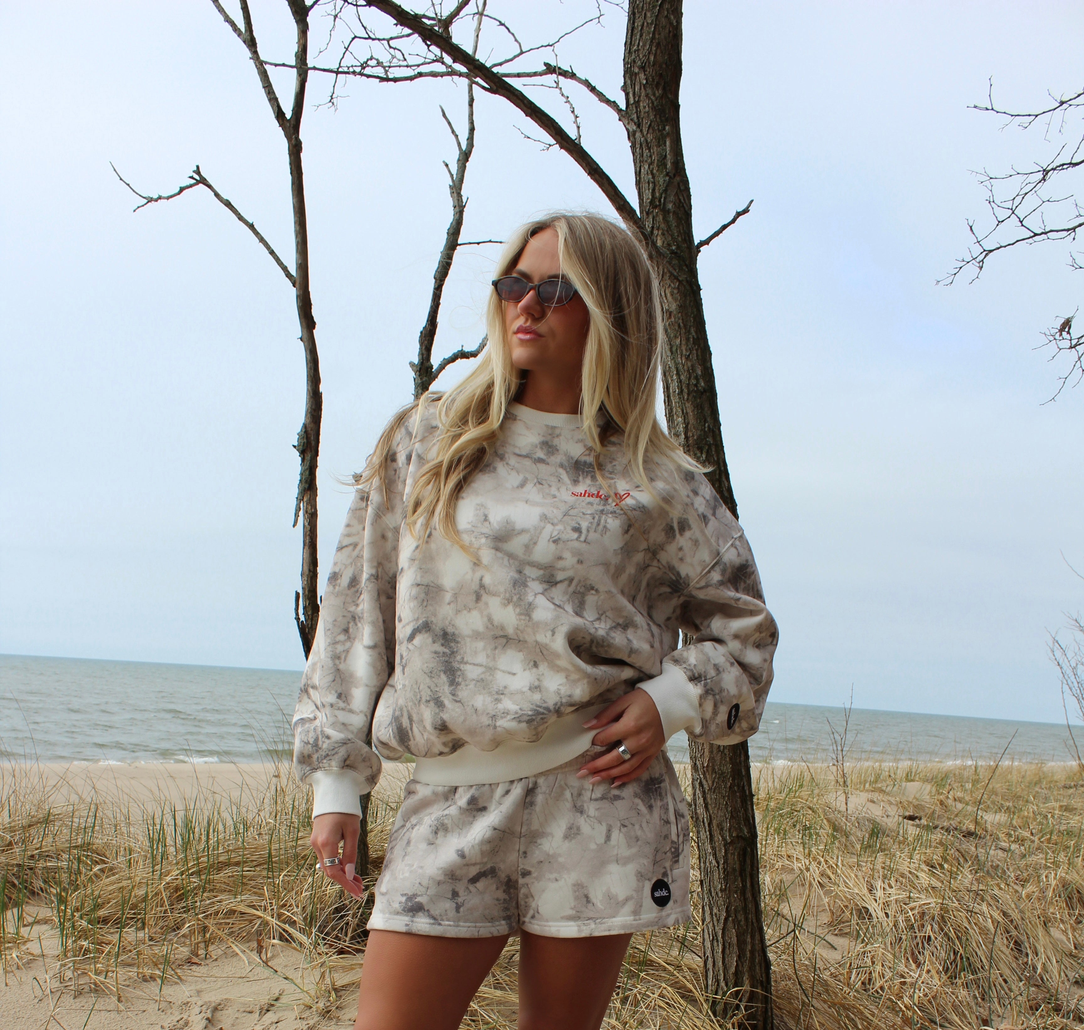 Woman in a  camo outfit standing on a beach with trees in the background