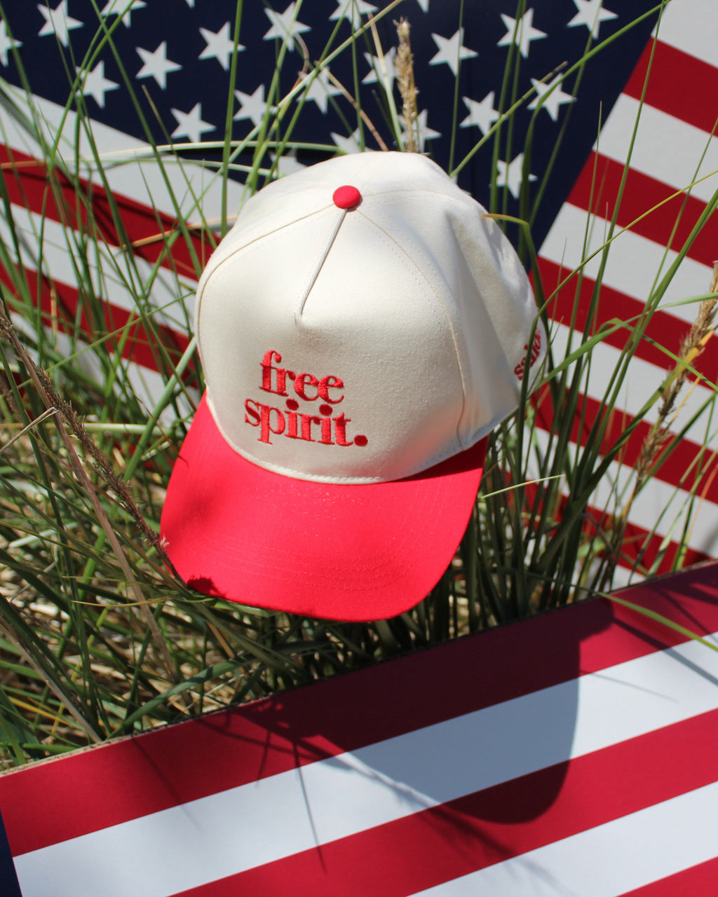 White cap with red brim and 'free spirit' text on an American flag background