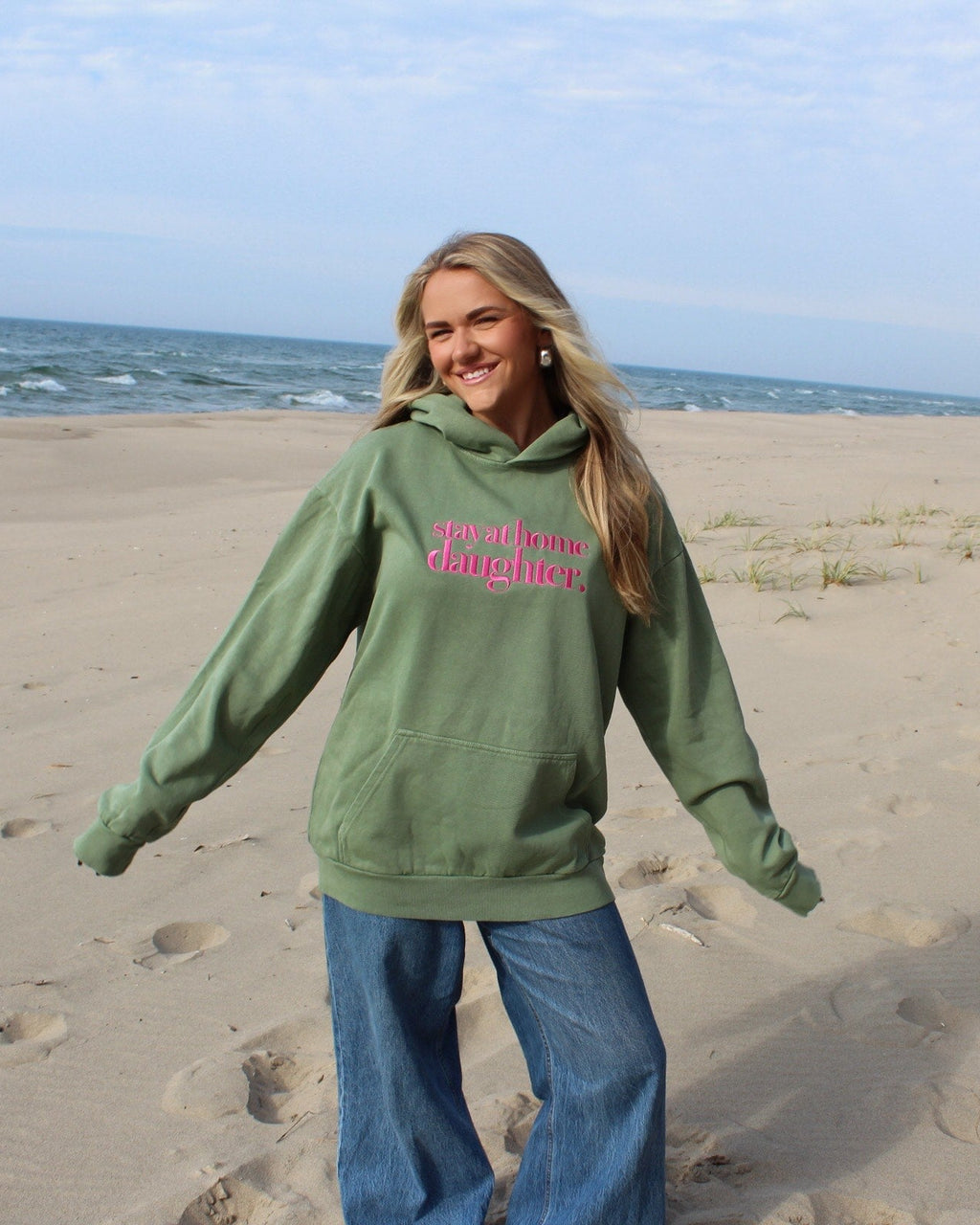 Person wearing a green hoodie with pink text on a beach