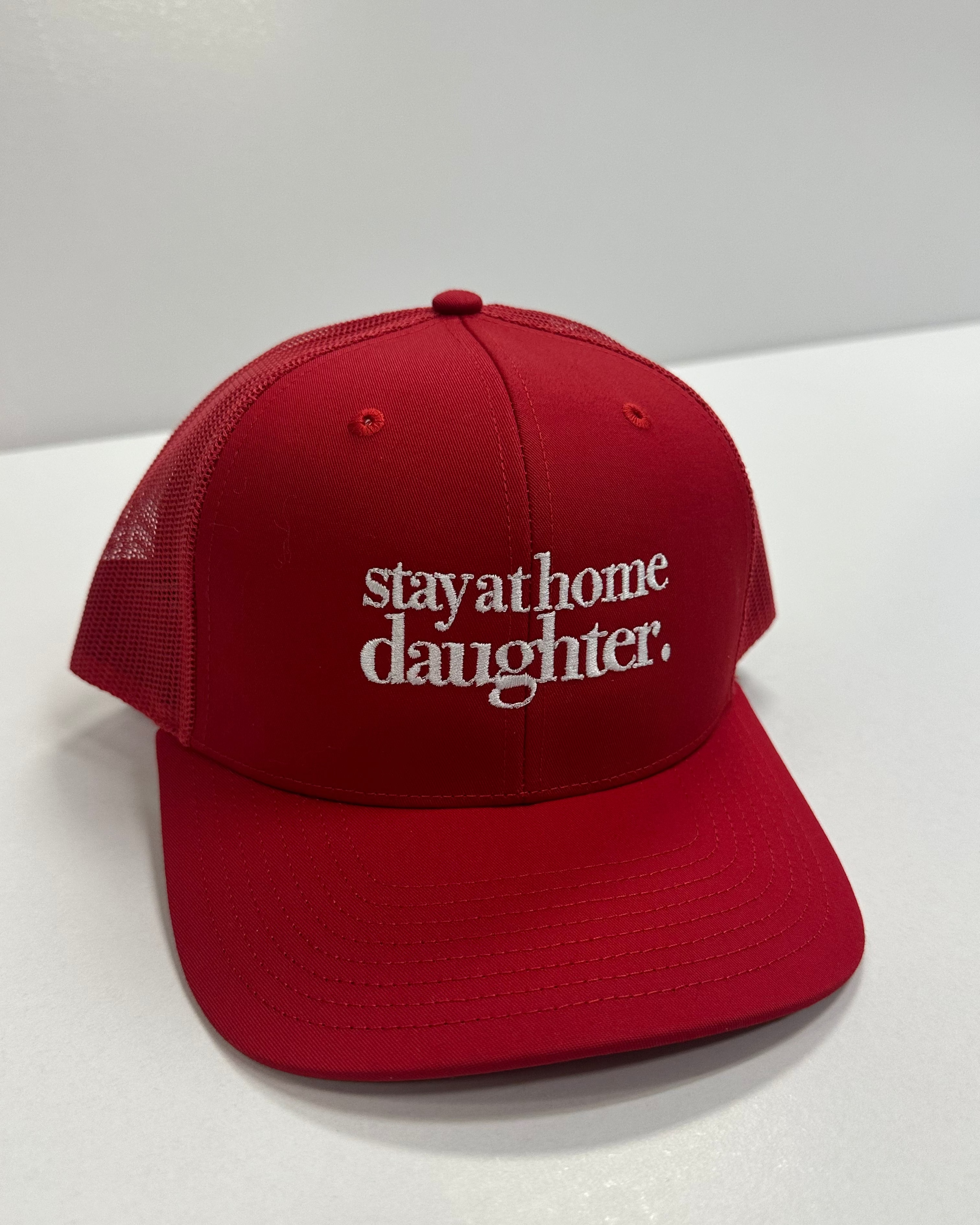 Red cap with 'stayathome daughter' text on a white surface