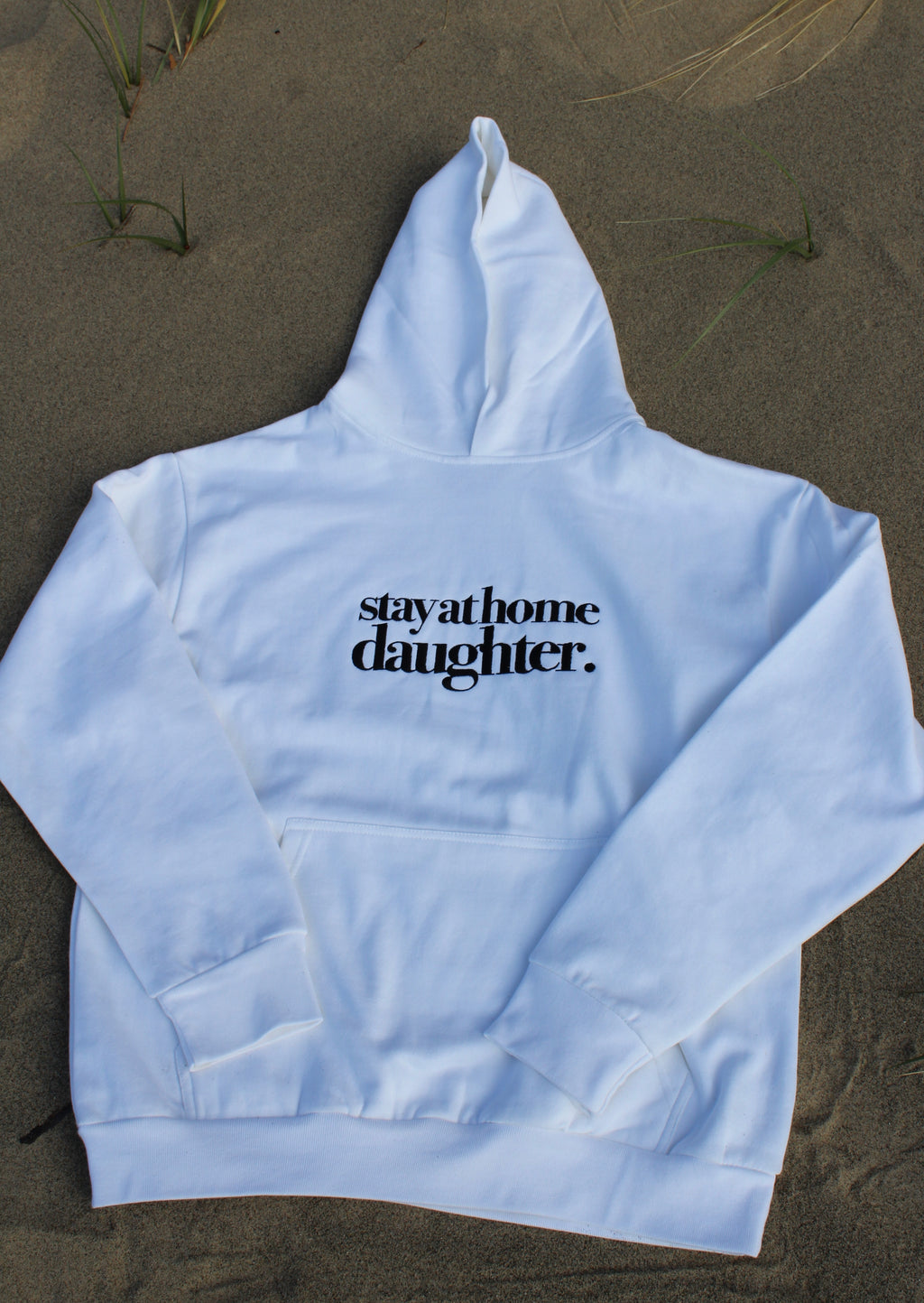White hoodie with 'stayathome daughter' text on a sandy background