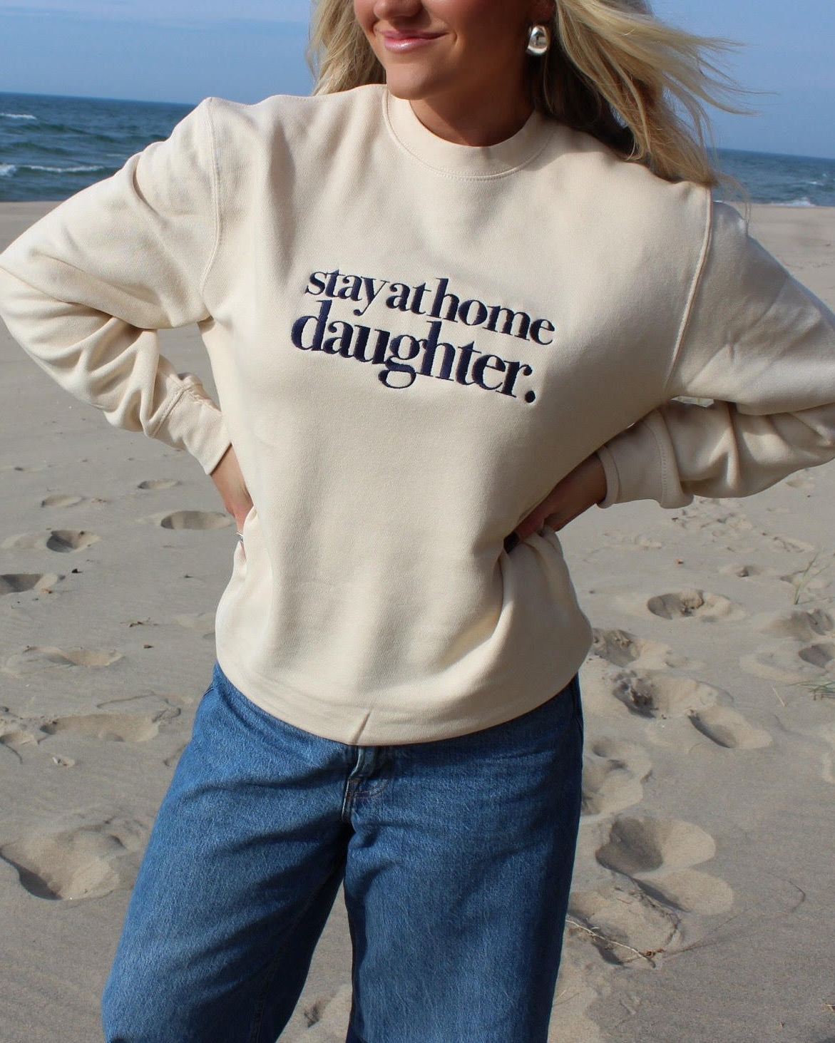 Person wearing a 'stay at home daughter' sweatshirt on a beach