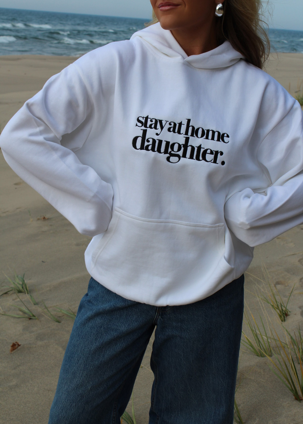 Person wearing a white hoodie with 'stay at home daughter' text on a beach.