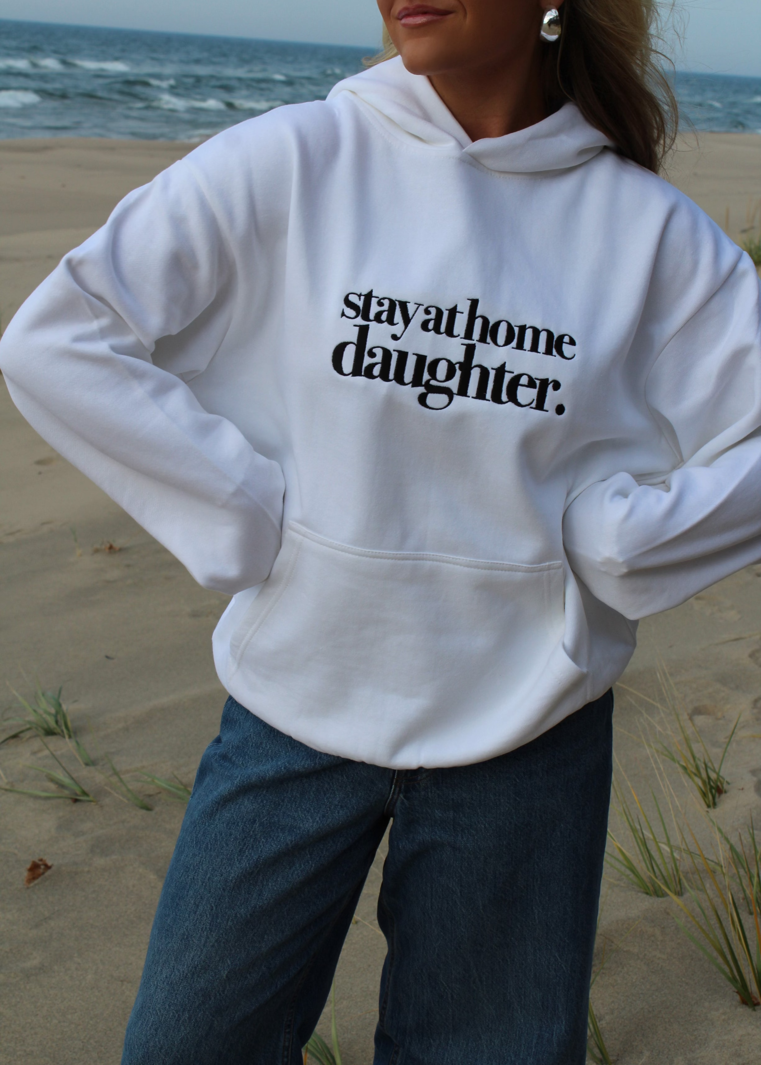 Person wearing a white hoodie with 'stay at home daughter' text on a beach.